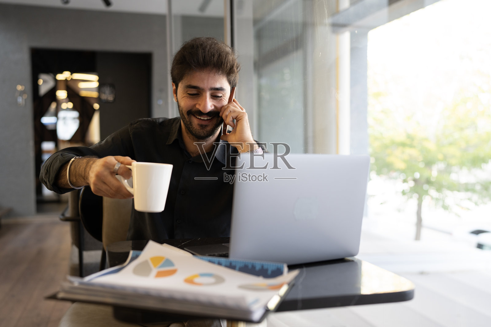 微笑的商人一边工作一边应对多项任务，手里还拿着咖啡照片摄影图片