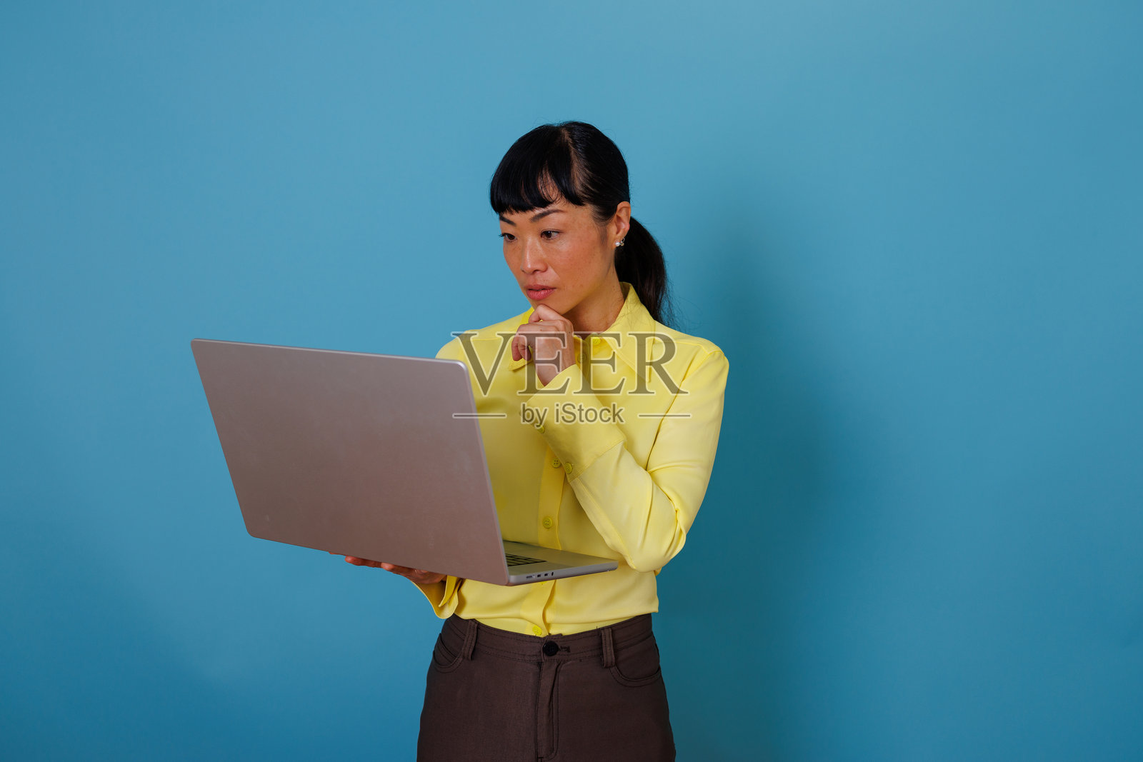 一位亚洲女商人正在使用笔记本电脑思考，在蓝色的工作室背景下构思新项目照片摄影图片