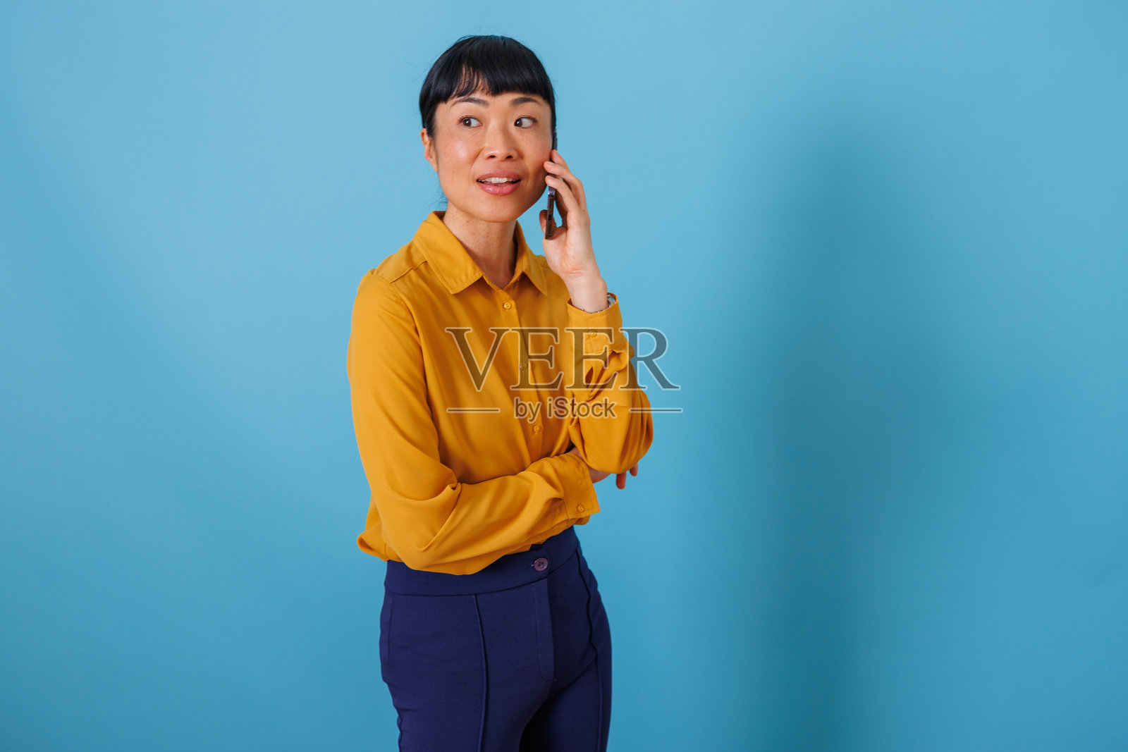 亚洲女性在蓝色背景上打电话，看向别处，进行专业对话照片摄影图片