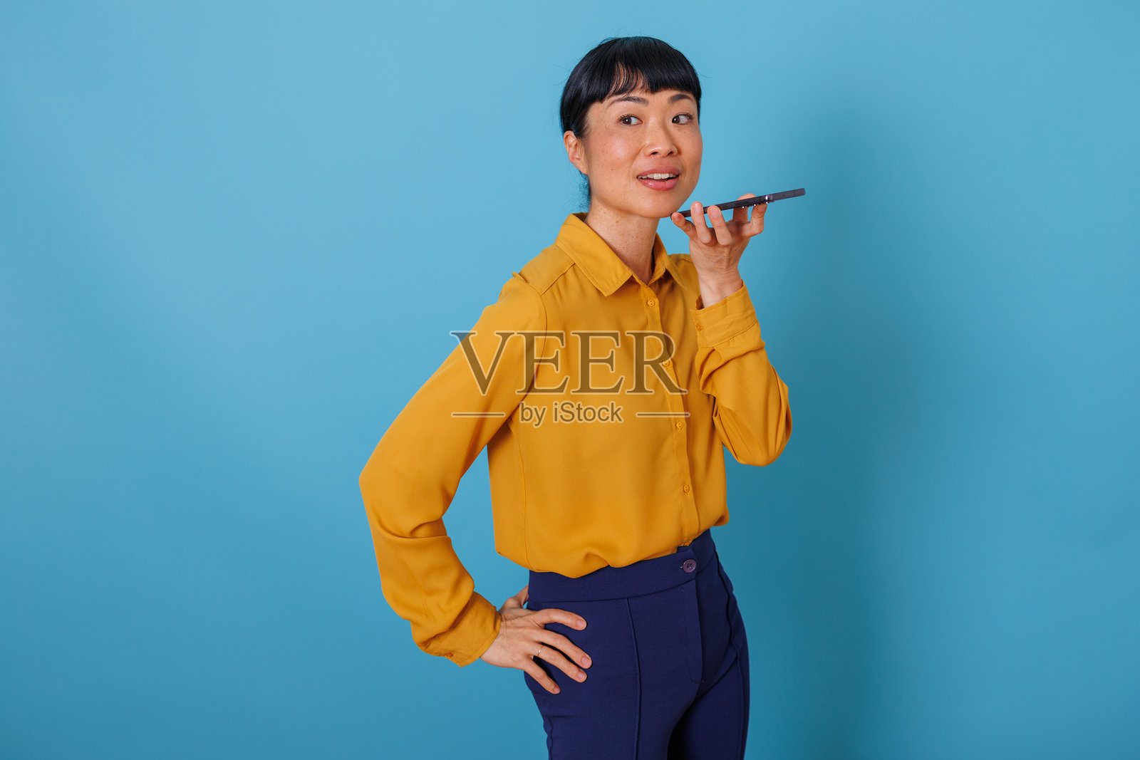 一位自信的年轻亚洲女性正在免提使用智能手机进行语音通话或录制消息照片摄影图片