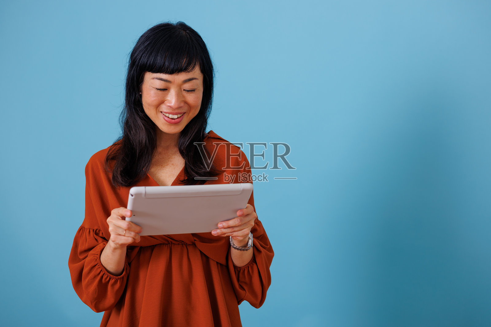 女子微笑着，在蓝色背景下使用平板电脑。她正享受着网络内容和现代科技。照片摄影图片