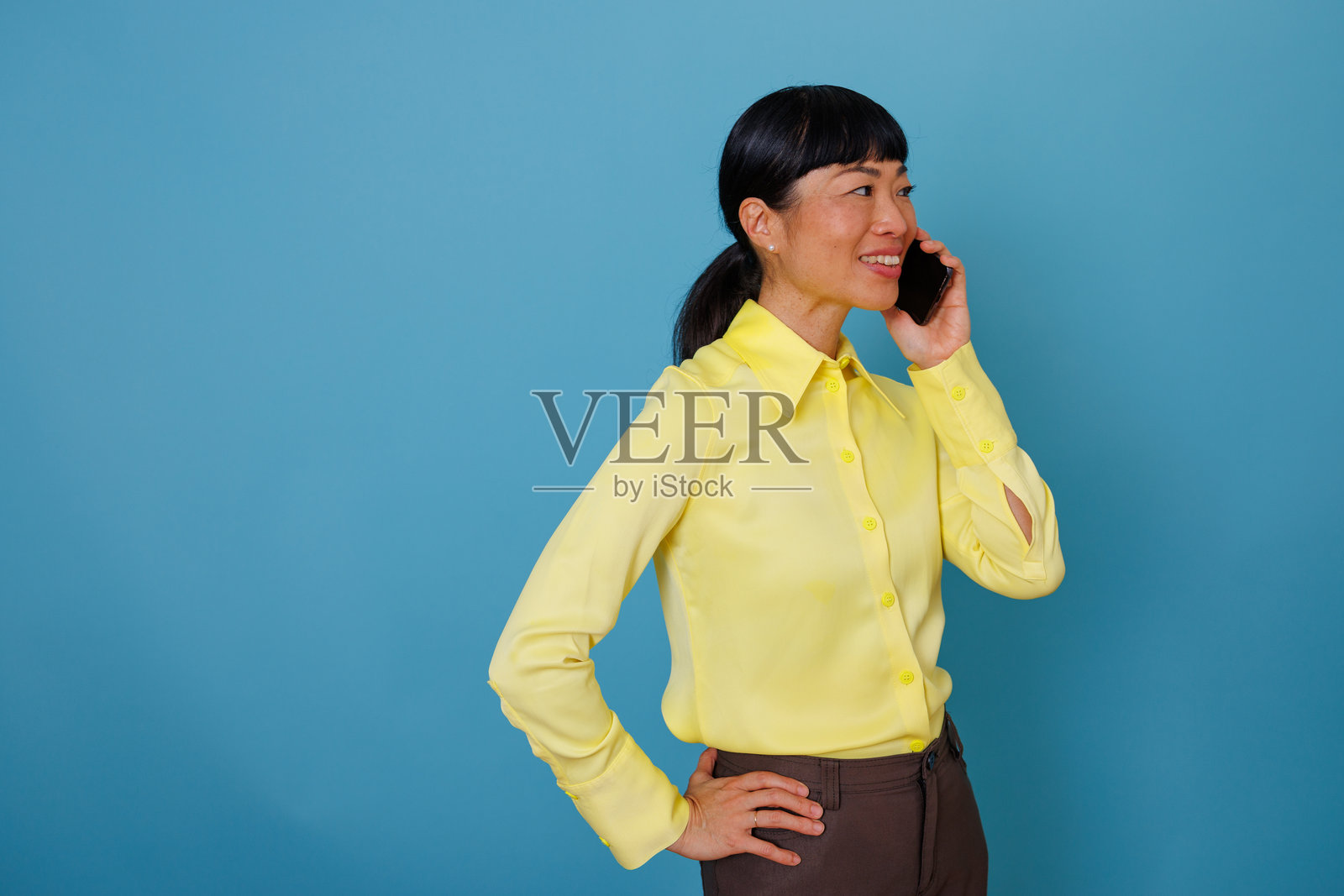 一位穿着黄色衬衫的亚洲女商人在自信地微笑着打电话照片摄影图片