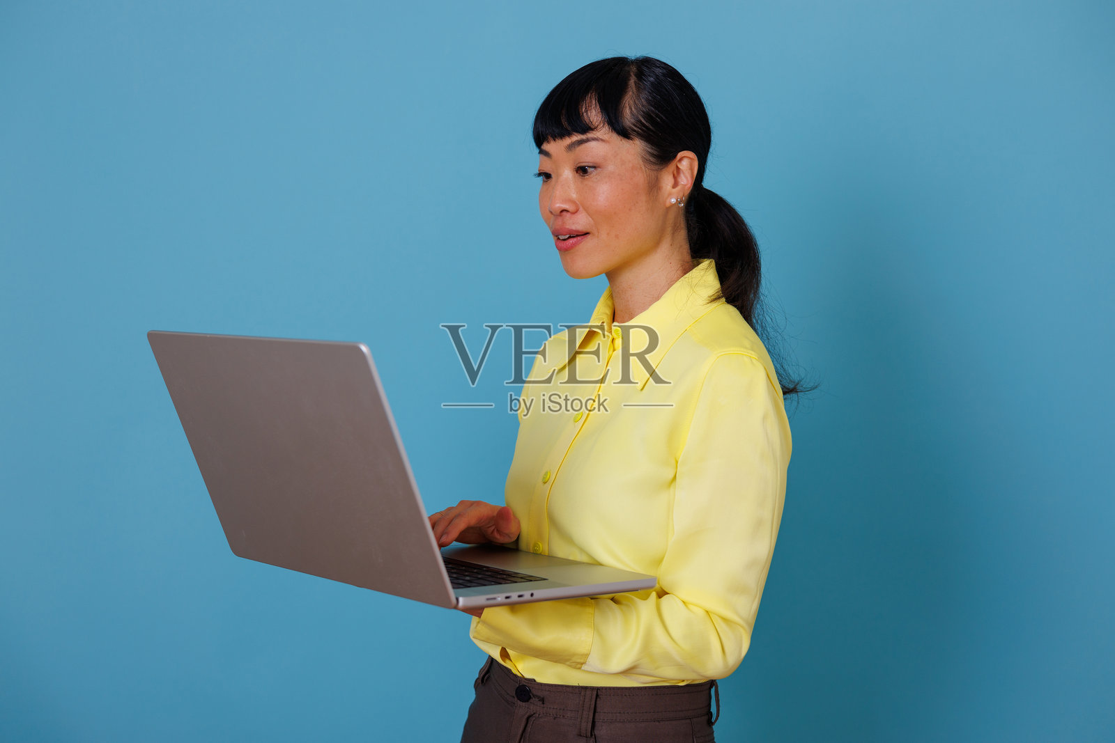 一位专业的亚洲女性站着，手持笔记本电脑正在打字，聚焦于科技、商务和远程办公。照片摄影图片