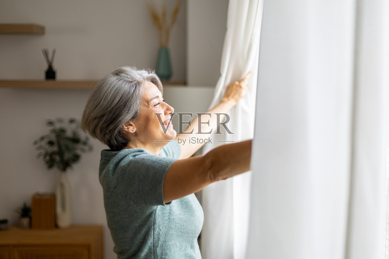 快乐的成熟的女性拉开卧室窗帘照片摄影图片