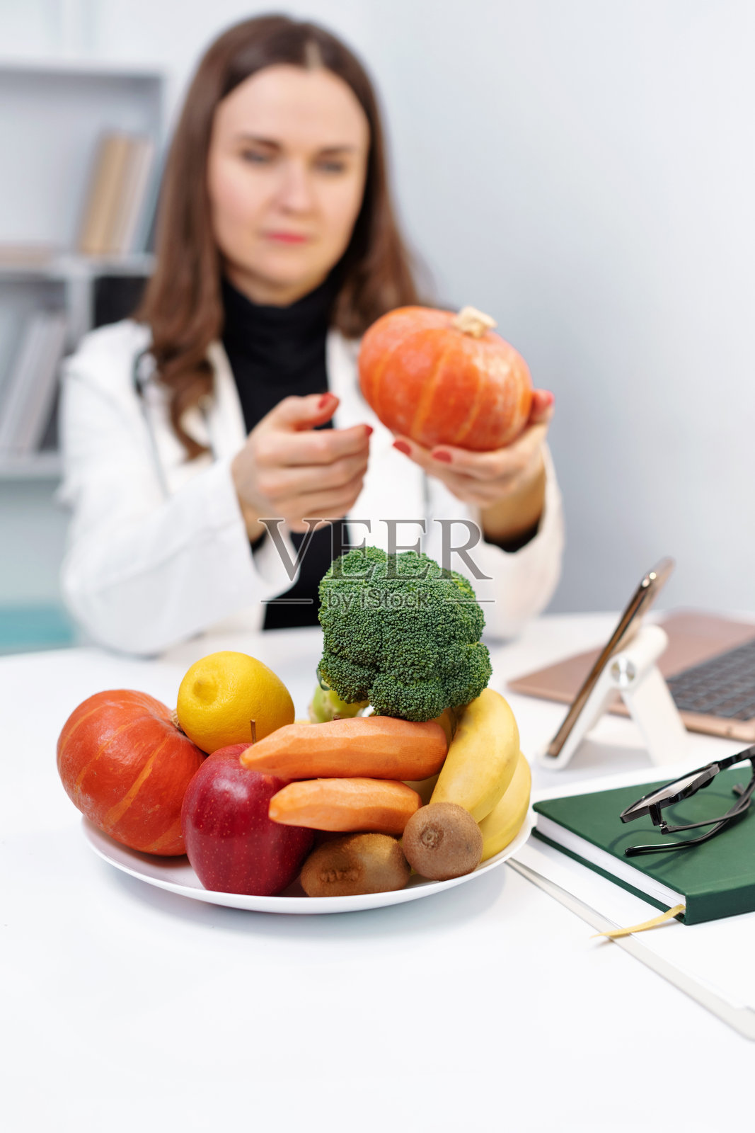 桌上的蔬菜特写。医生或营养师通过笔记本电脑与病人进行远程沟通，在线咨询。医疗保健咨询。远程医疗。照片摄影图片