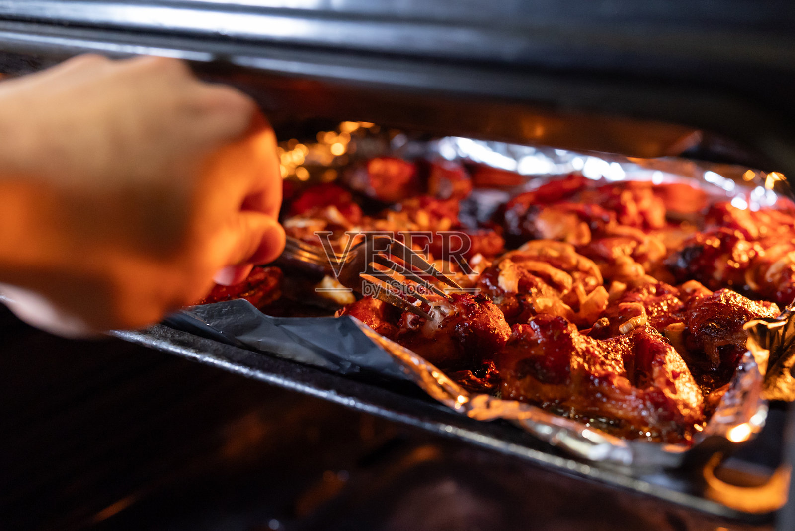 一只手正用叉子在烤箱中检查烤鸡翅的熟度照片摄影图片