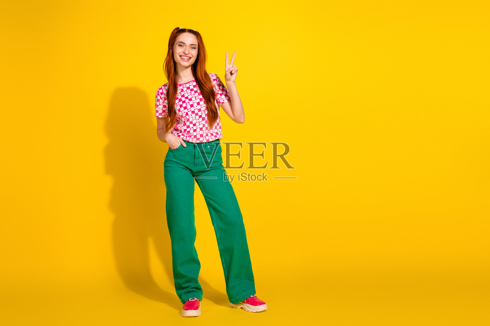 身穿色彩鲜艳休闲装的年轻女孩，对着明亮的黄色背景微笑并比出胜利手势照片摄影图片