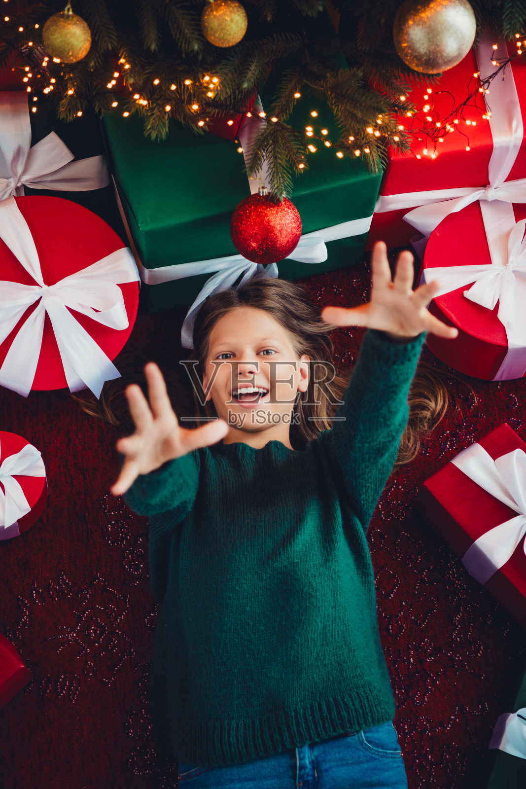 温馨的节日场景中，一个快乐的孩子在充满礼物的圣诞树、彩灯和节日装饰的家中向上伸手。照片摄影图片