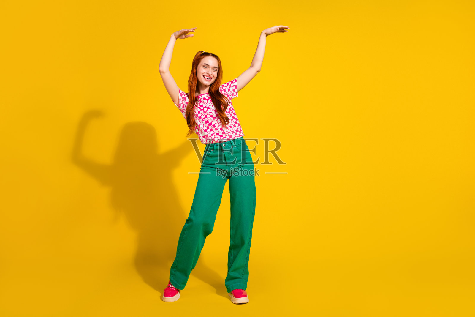身穿格子粉色T恤和绿色裤子的年轻女孩，在鲜亮的黄色背景前展现出活泼的时尚瞬间，非常适合广告和生活方式类图片照片摄影图片