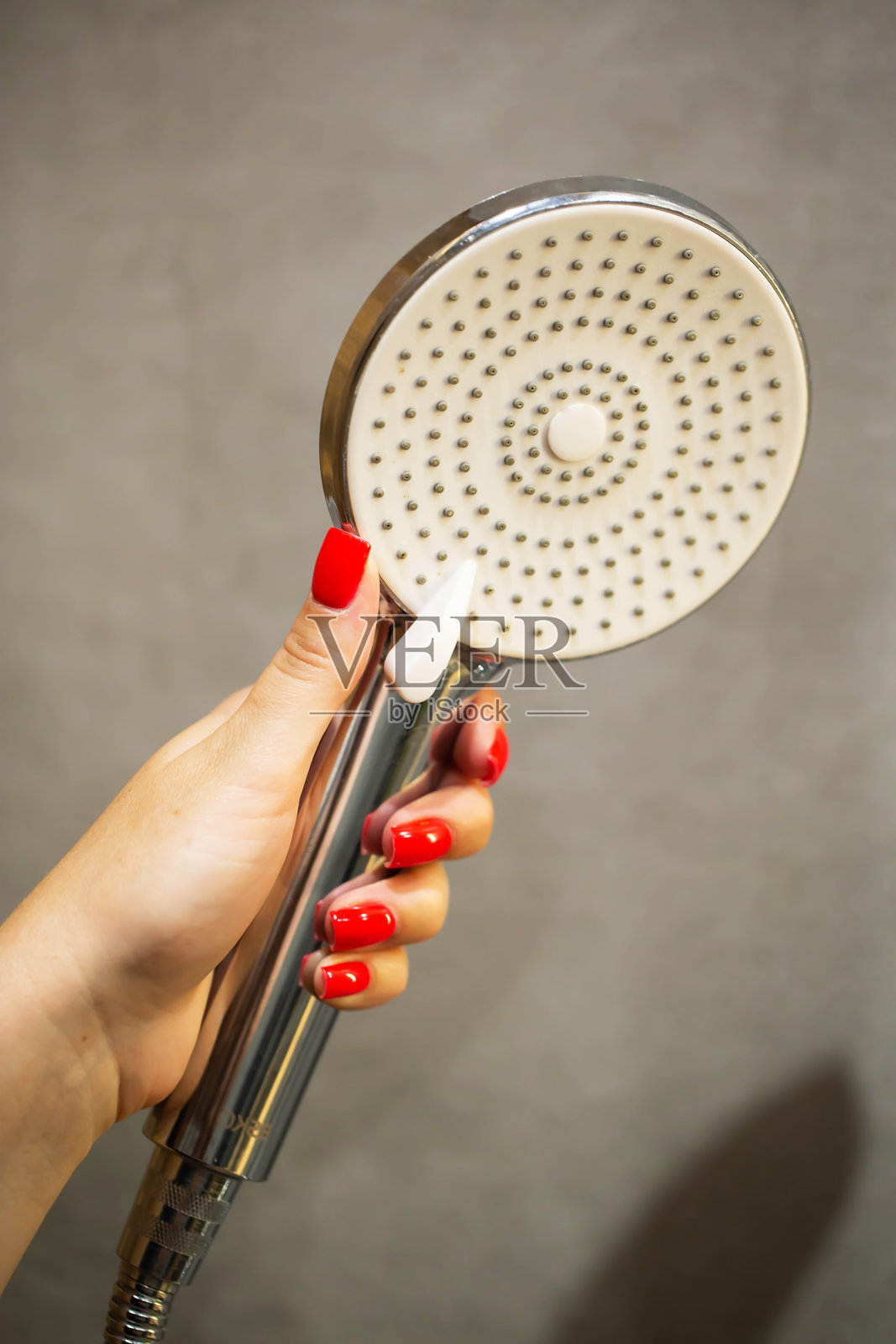 手部特写，一名涂着红色指甲油的女性手持现代淋浴喷头，行业照片摄影图片