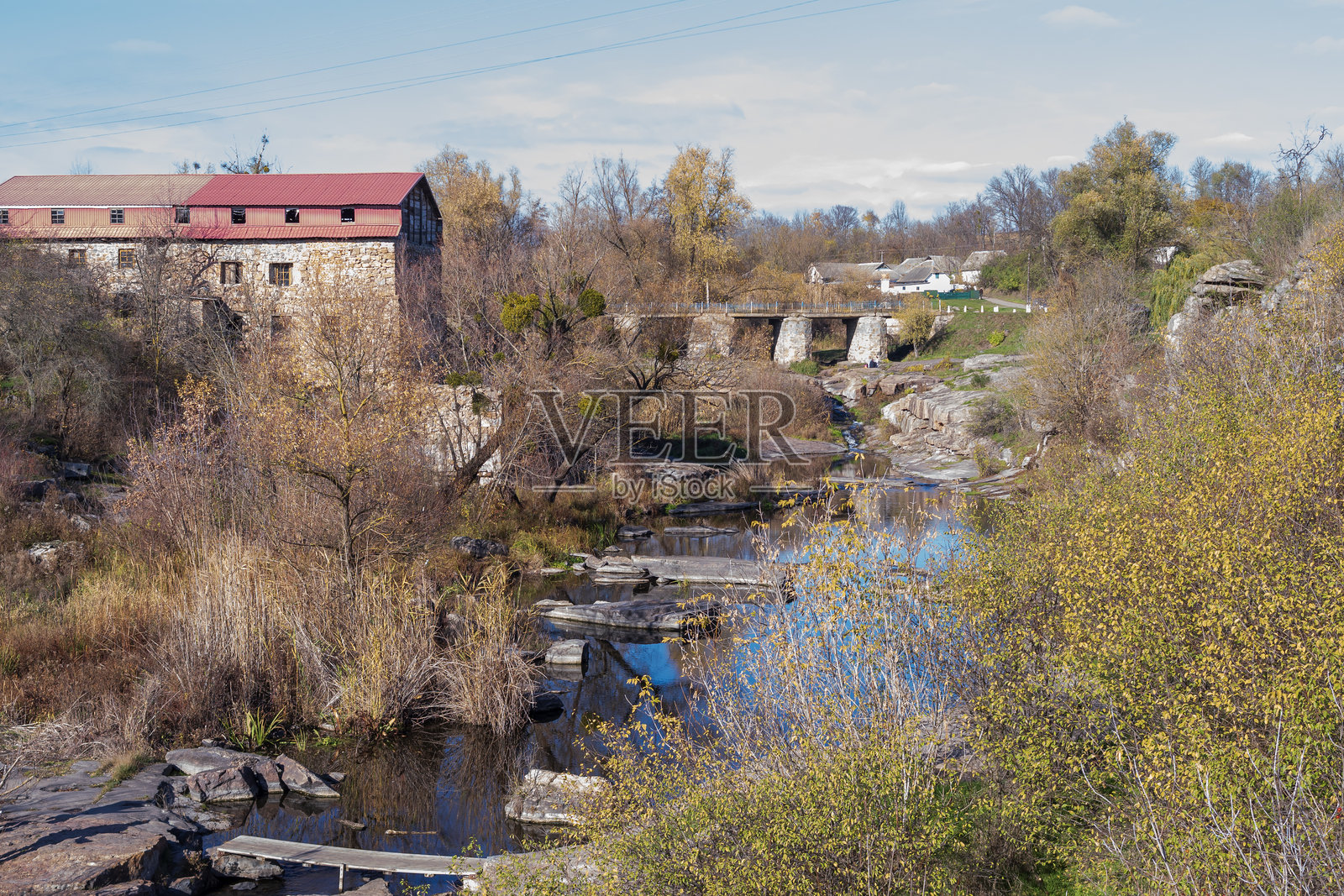 风景如画的秋季景色，描绘了一座历史悠久的石磨坊、一座古老的桥梁和一条岩石河流，河水静谧，伴有枯萎的植被和乡村自然肌理。照片摄影图片
