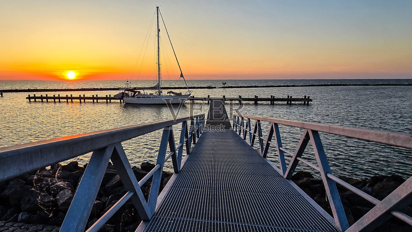 夕阳映照着码头，帆船和栈桥在水面倒影中摇曳照片摄影图片