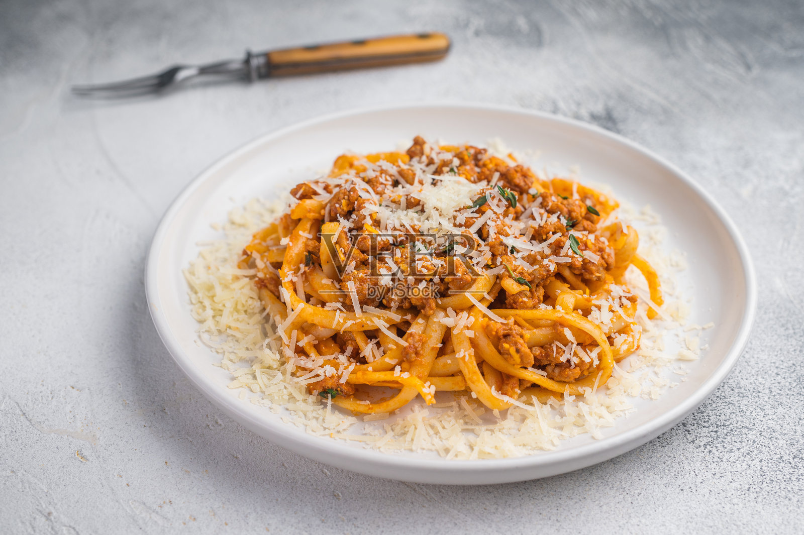 美味的肉酱意面撒上帕玛森芝士，置于纹理灰背景上，明亮干净的食物俯拍照片。照片摄影图片