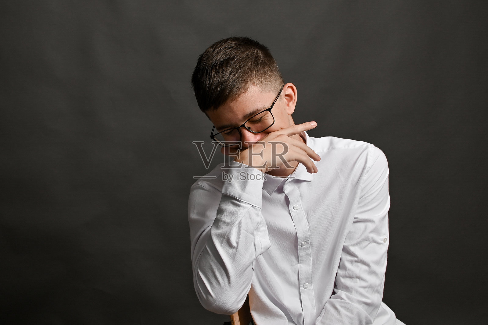 身穿白衬衫的年轻男子，手靠近嘴巴摆拍。照片摄影图片