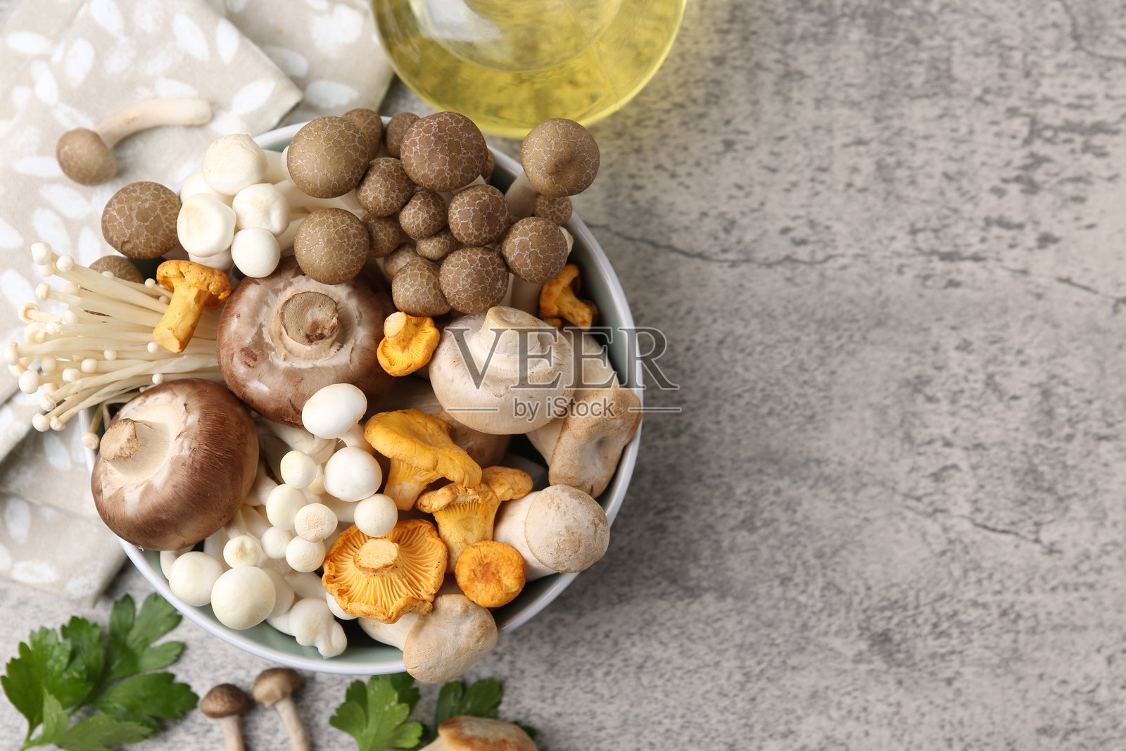 不同种类的生蘑菇放在碗里，配以欧芹和油，置于灰色纹理桌面上，俯视角度。留有文字空间照片摄影图片