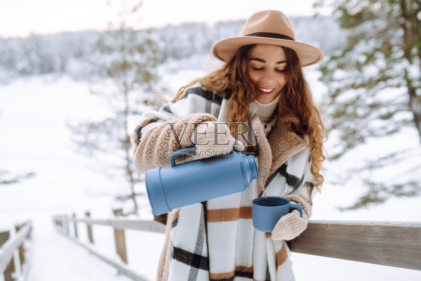 年轻女旅行者从蓝色保温瓶向马克杯中倒热饮的肖像。照片摄影图片