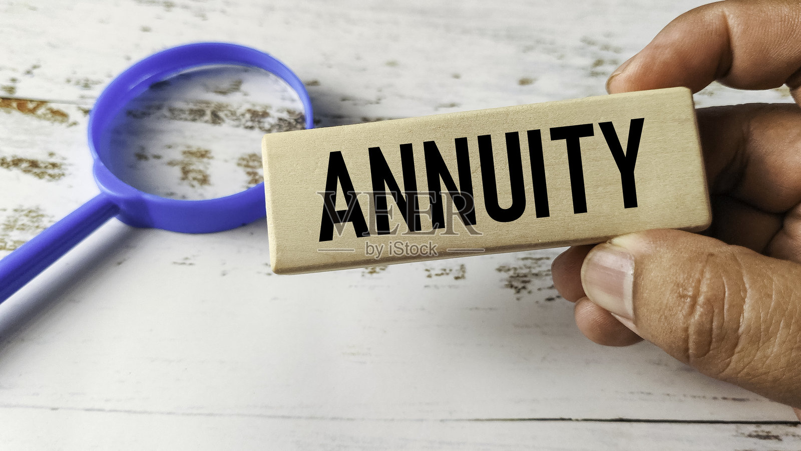 一只手拿着刻有“年金”的木块，旁边放着一个放大镜，代表退休储蓄和财务规划照片摄影图片