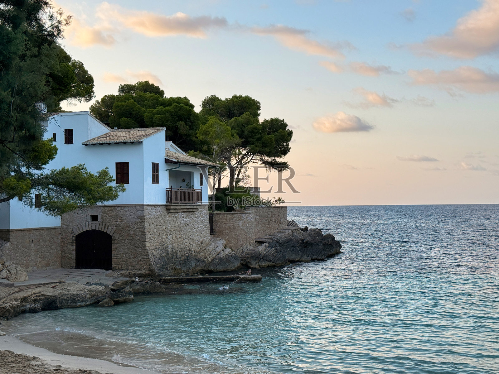 坐落在马略卡卡拉加特，一座小白房子矗立在俯瞰大海的岩石悬崖上照片摄影图片