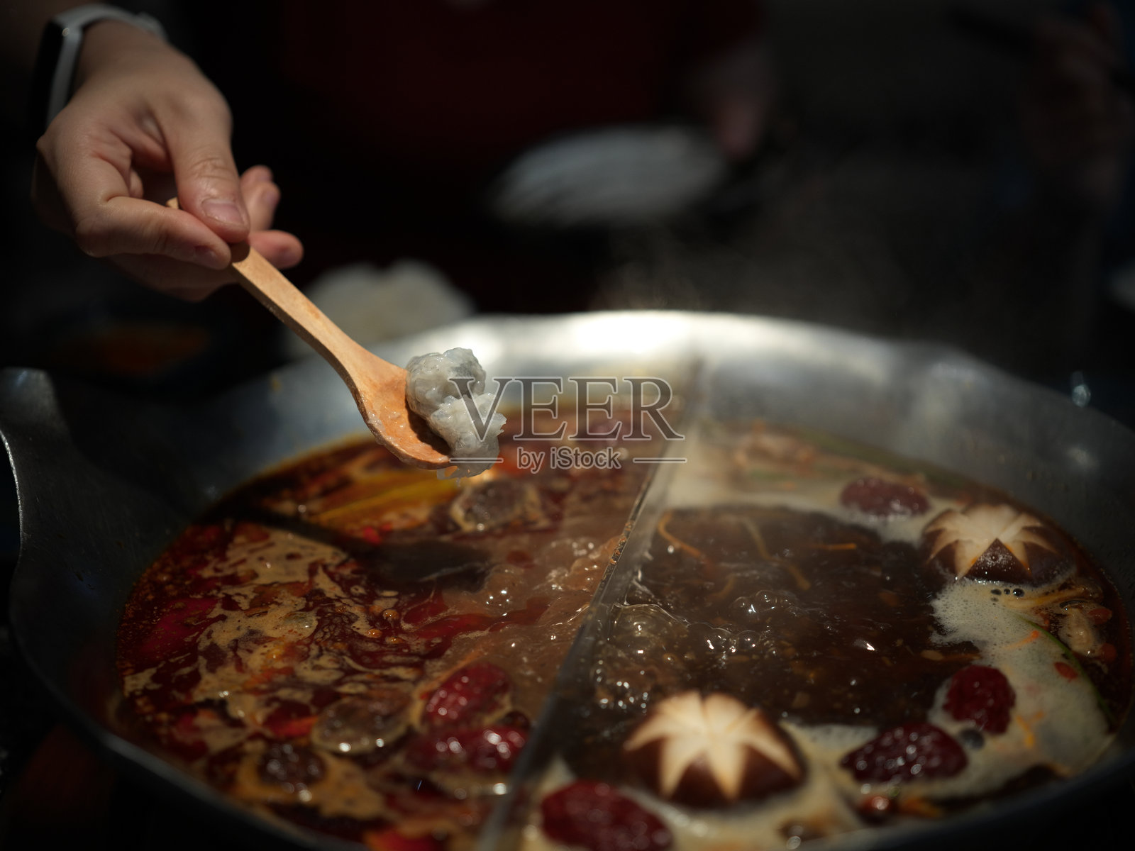 一个人用木勺从分隔的鸳鸯锅中舀取食材，锅内有麻辣和清汤两种汤底照片摄影图片