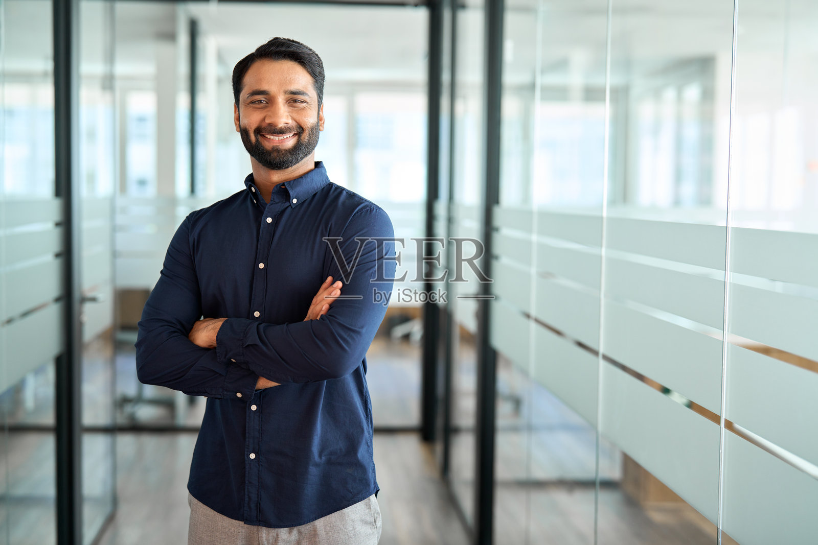 一位快乐的印度商人，职业领袖，双臂交叉站立在办公室里。照片摄影图片