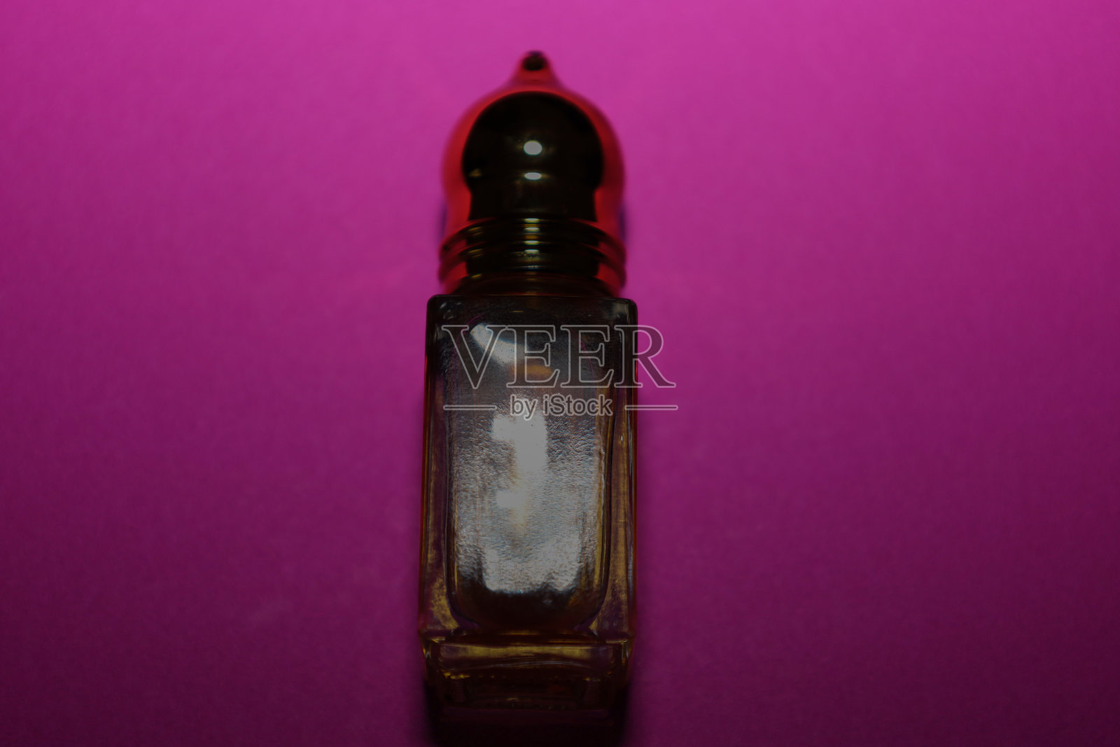 一款带有光泽金色瓶盖的迷你矩形玻璃香水瓶或精油瓶，垂直放置在明亮的紫粉色背景上。时尚的设计和鲜明的对比强调了优雅，并与芳香疗法、化妆品和精选产品相关。照片摄影图片