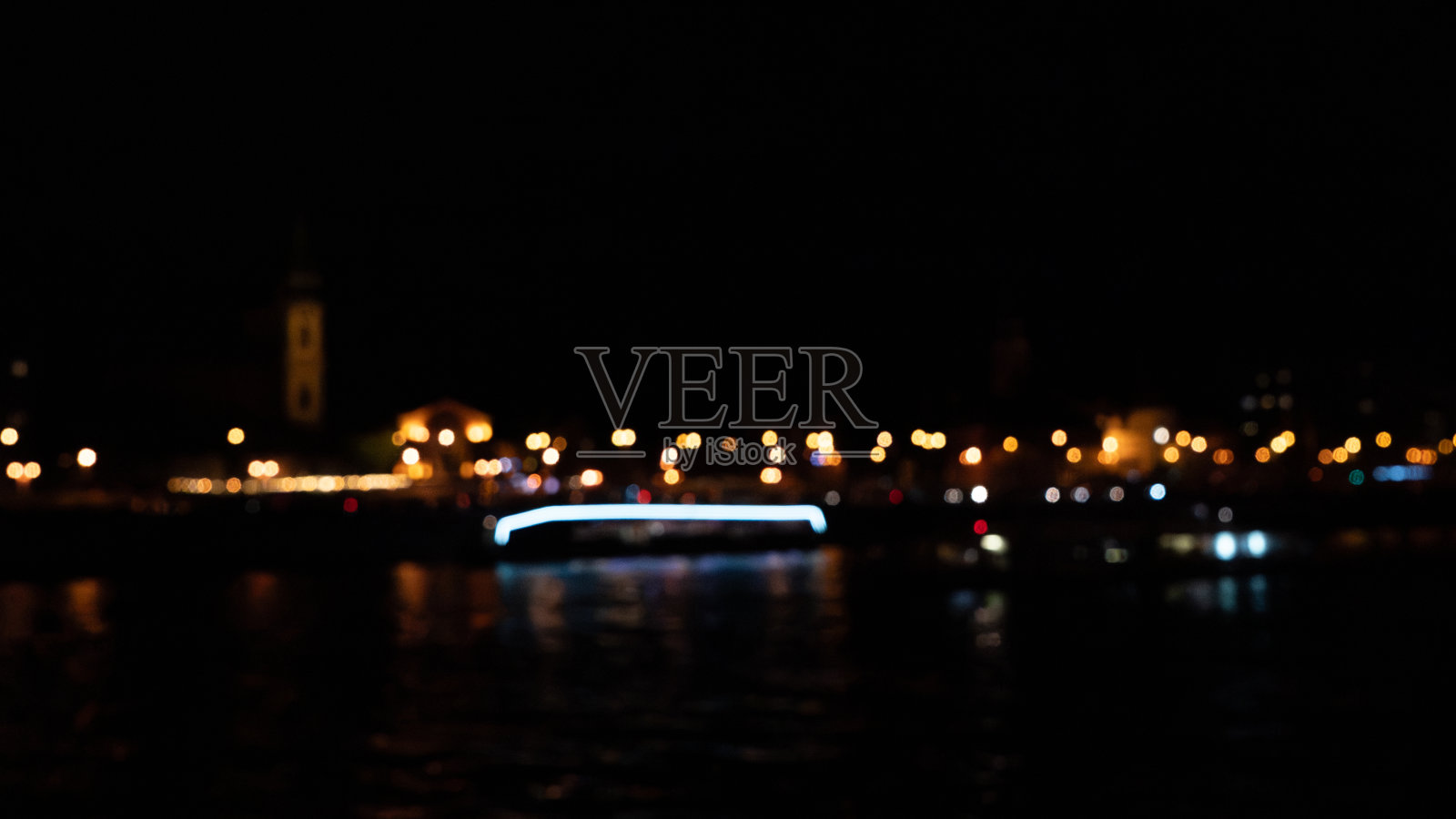 布达佩斯，匈牙利。夜间城市环境中，模糊的橙色城市灯光在黑暗水面上形成散景效果的反射。照片摄影图片