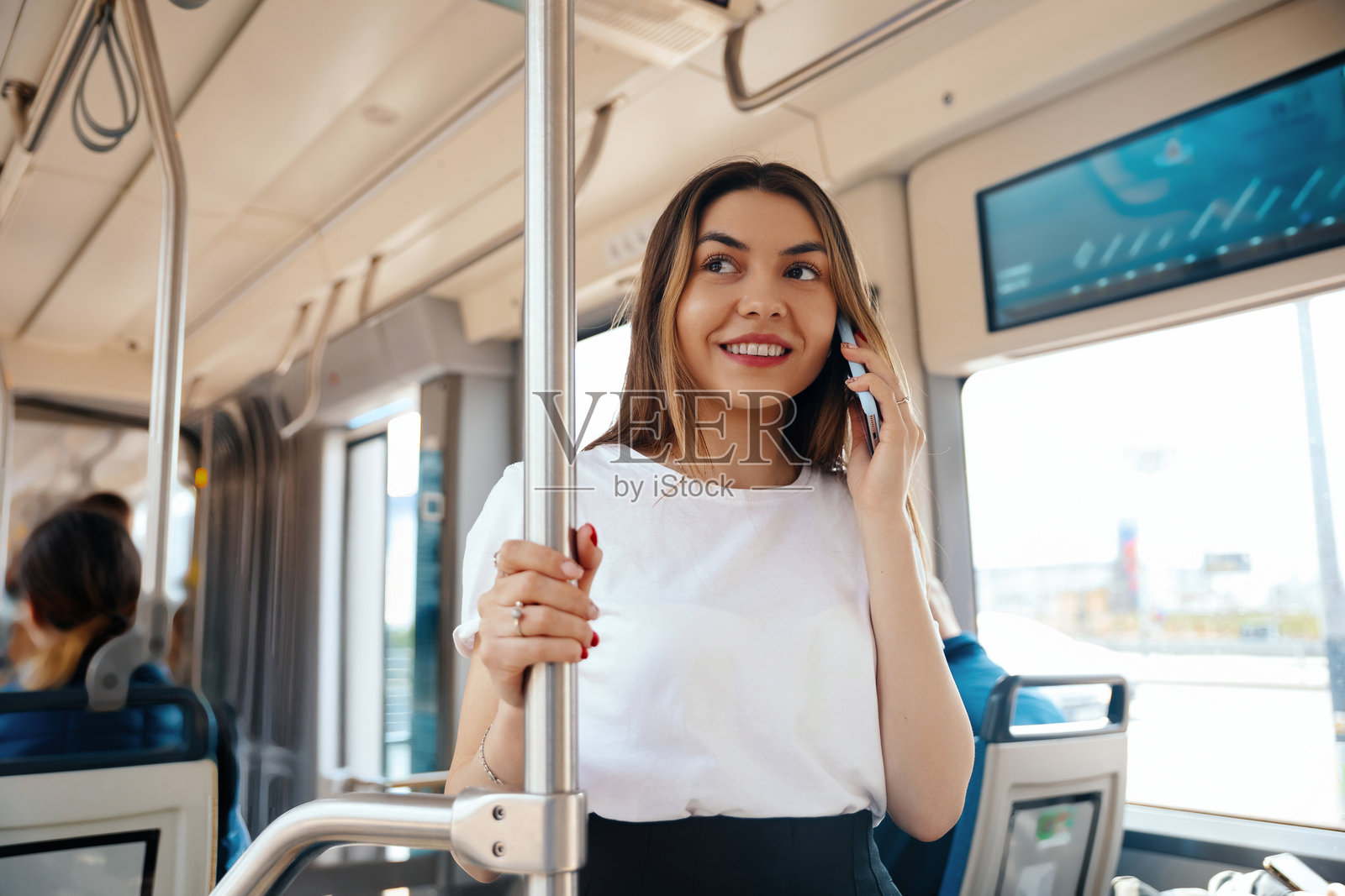 白天，一位年轻女子站在现代城市的公交车上打电话照片摄影图片