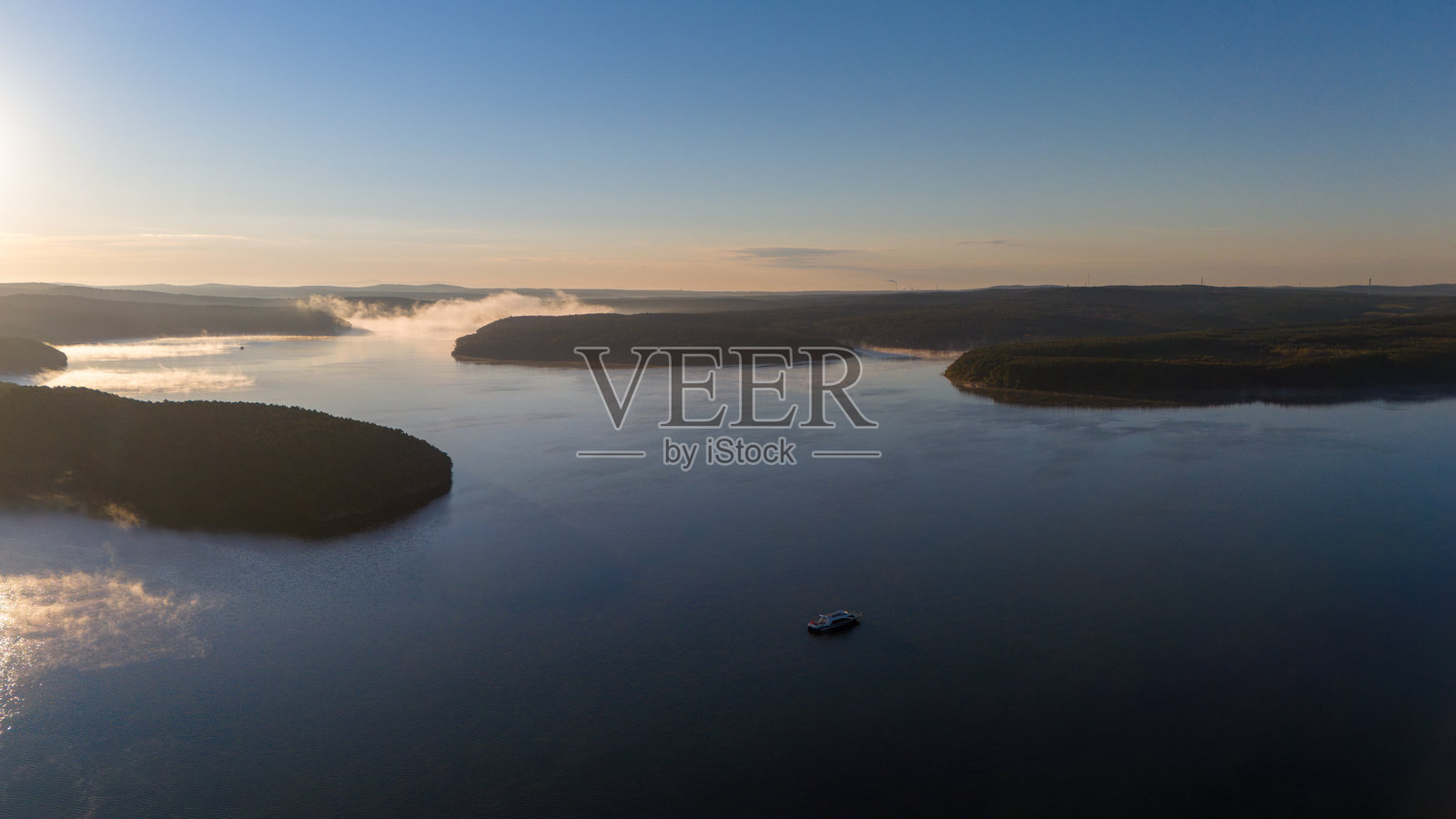 晨雾笼罩水面的宁静湖泊，四周环绕着森林的鸟瞰图照片摄影图片