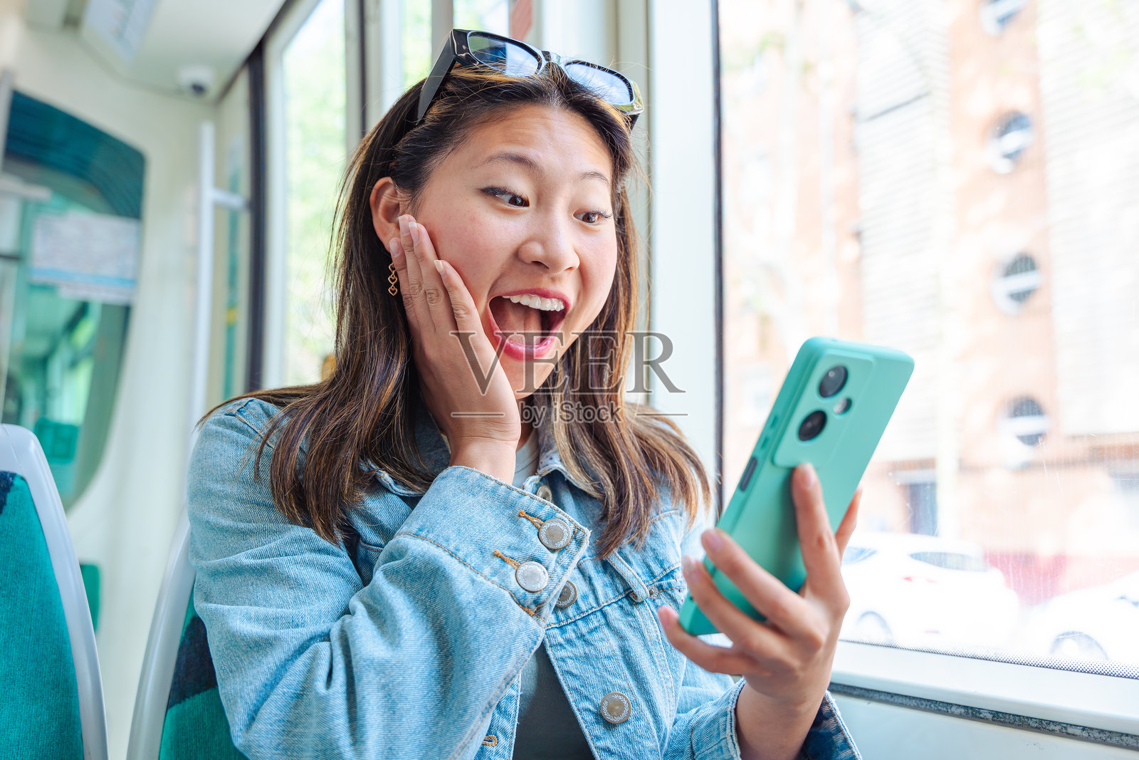 一名兴奋的女子在公共交通工具上看着智能手机，脸上露出惊讶的表情。照片摄影图片