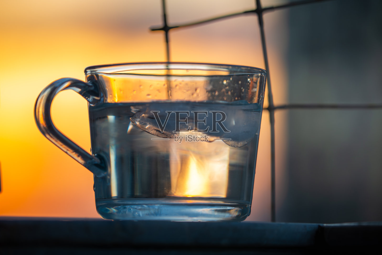 日落背景下，透明玻璃杯中冰块与水的宁静场景照片摄影图片