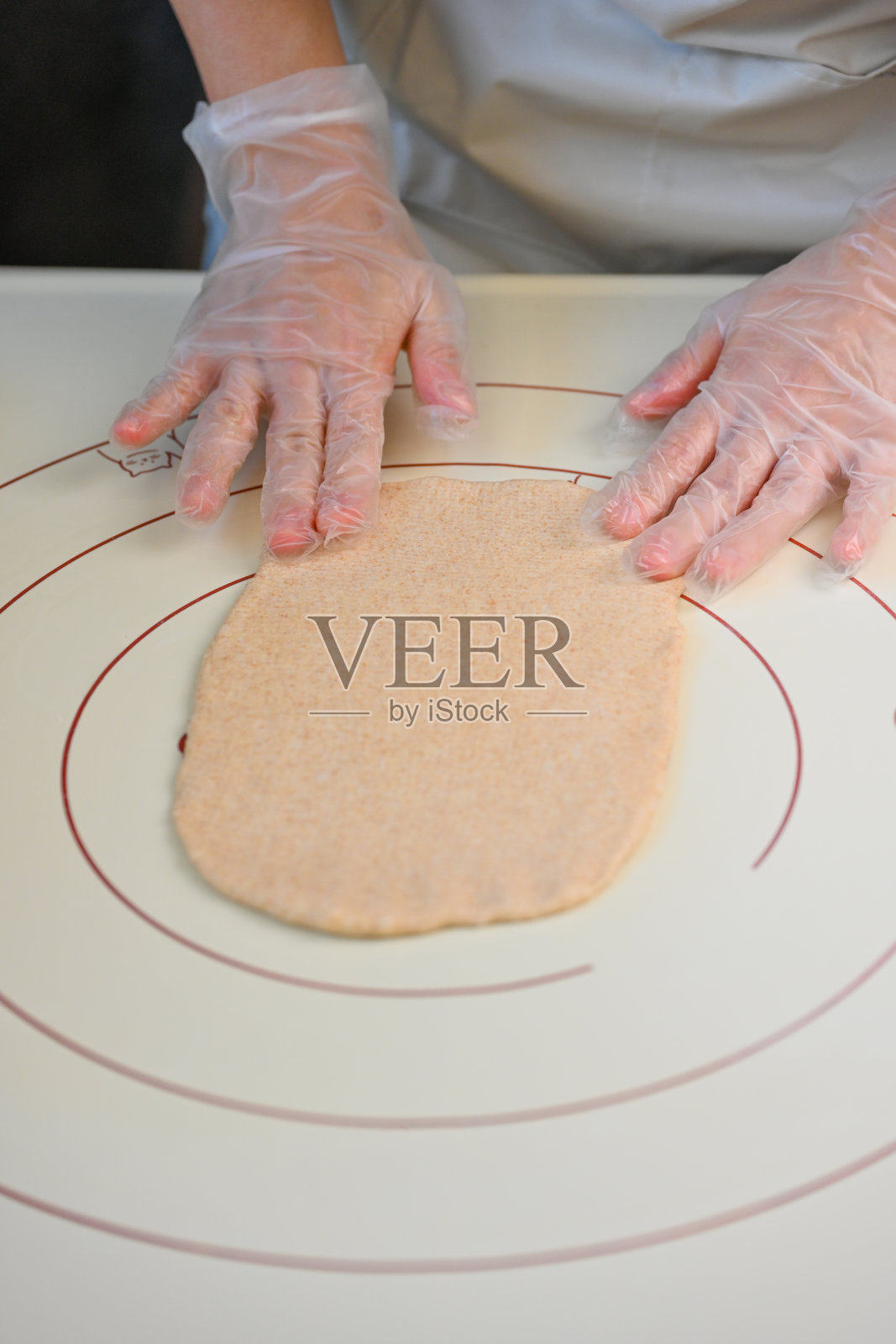 戴着一次性手套的手在带有测量圆圈和可爱动物插图的烘焙垫上压平面团照片摄影图片