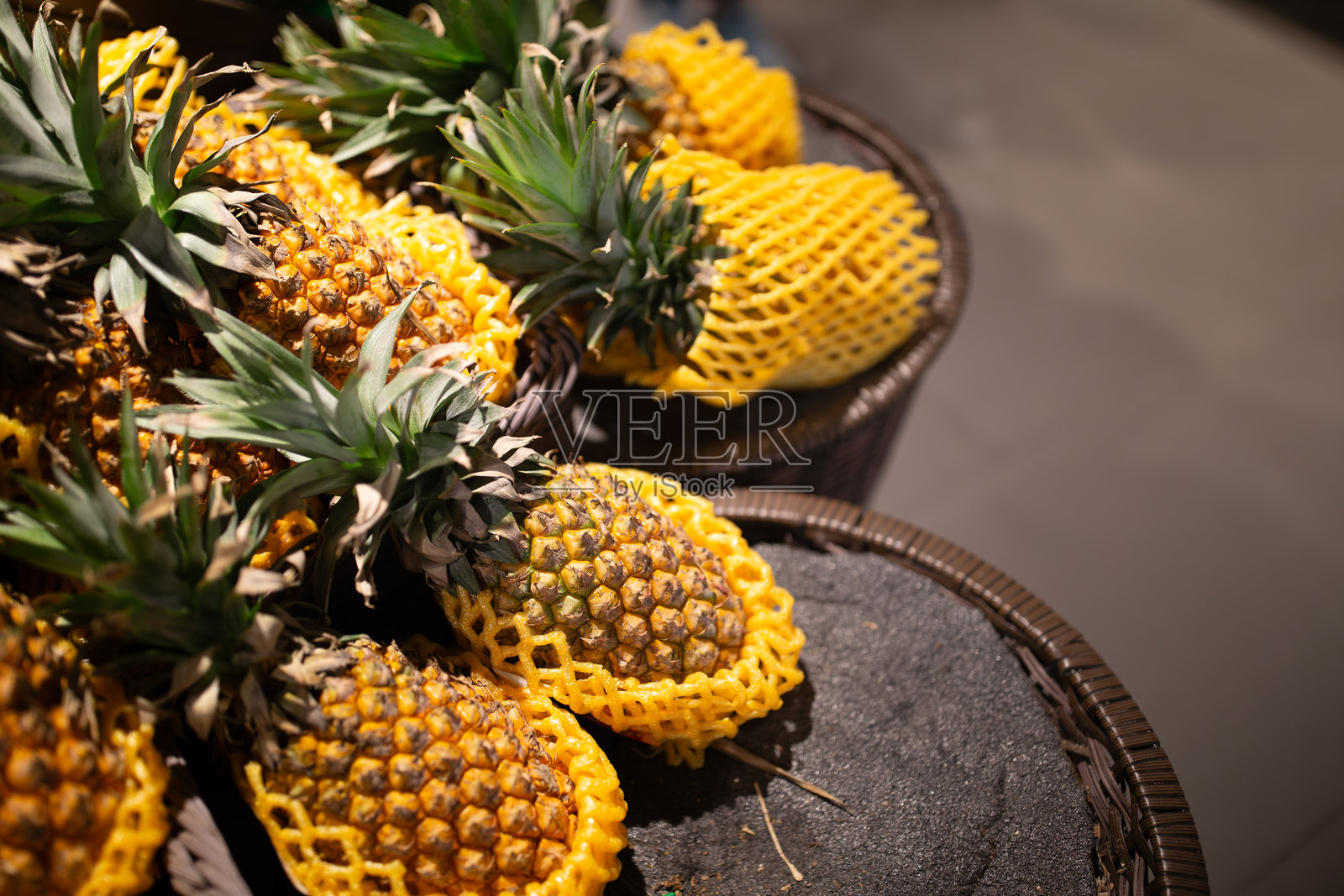篮子里展示着新鲜的菠萝，并用黄色网套保护着照片摄影图片