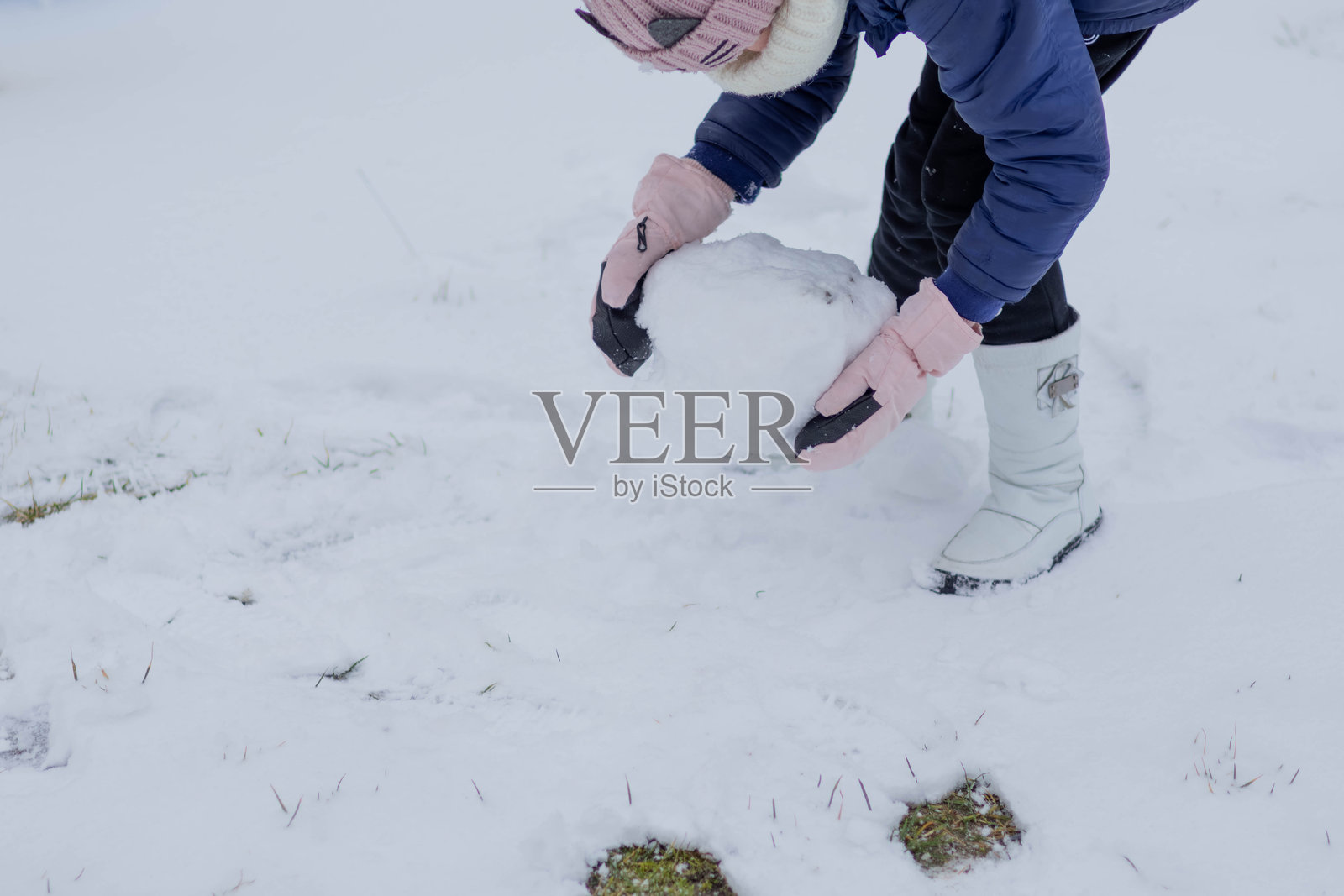 冬天，一个孩子在雪地里滚雪球照片摄影图片