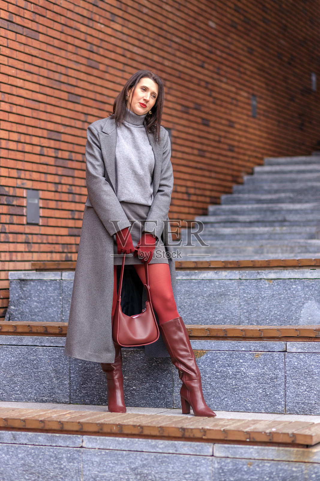 一位棕发女子身穿灰色外套，搭配酒红色配饰，漫步在城市秋日街头。穿着鲜艳的秋季服装。照片摄影图片