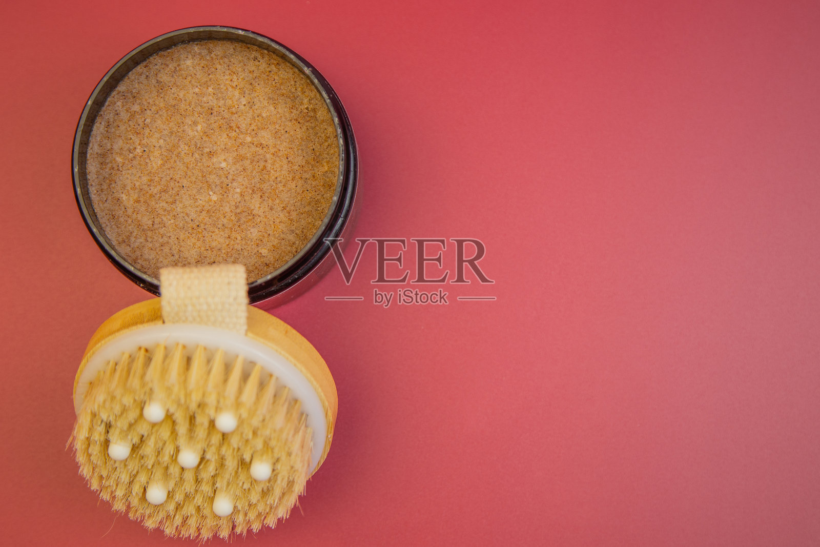 水疗护理必备品，包括一罐棕色糖磨砂膏和一把天然鬃毛身体刷，背景为鲜艳的粉红色，留有设计空间照片摄影图片