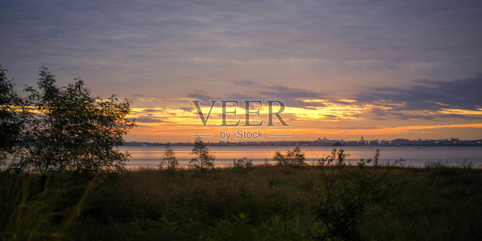 湖面上宁静的日落景色，远方是城市剪影和金色天空照片摄影图片