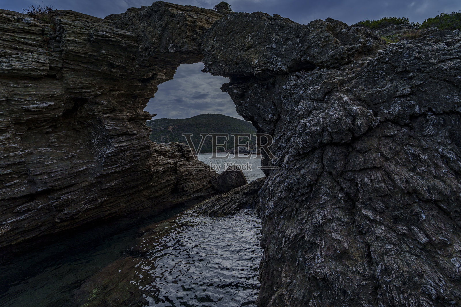 崎岖海岸悬崖上的深色海蚀拱门照片摄影图片