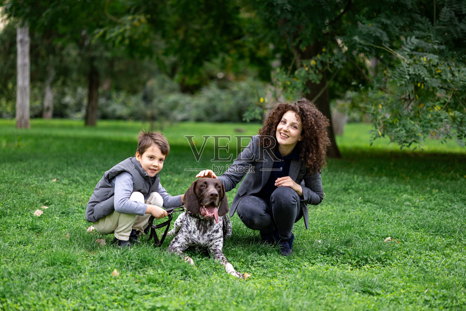 一位母亲和她的儿子以及他们的狗在绿色公园里照片摄影图片