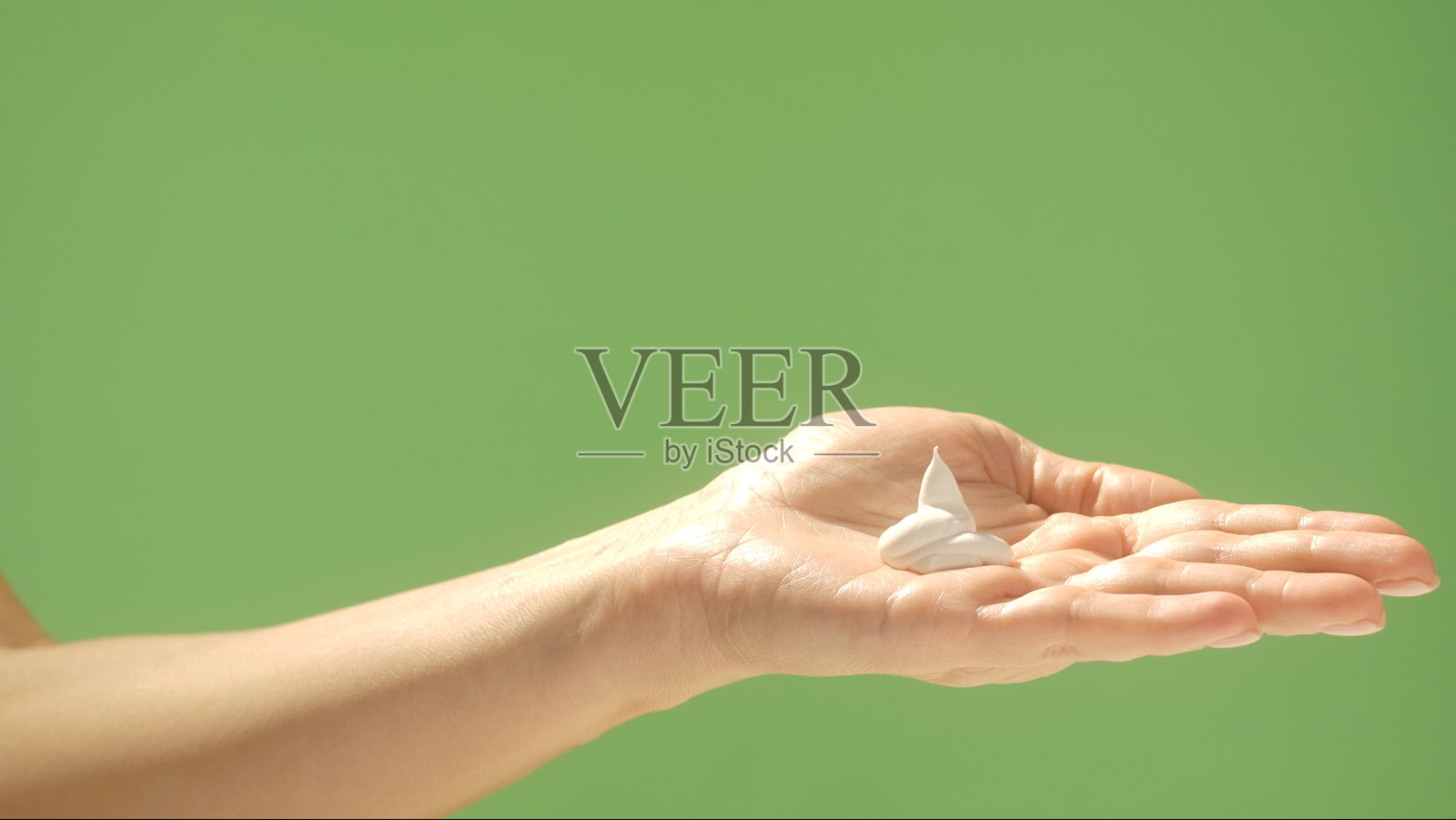 手持面霜，背景为简单的绿色照片摄影图片