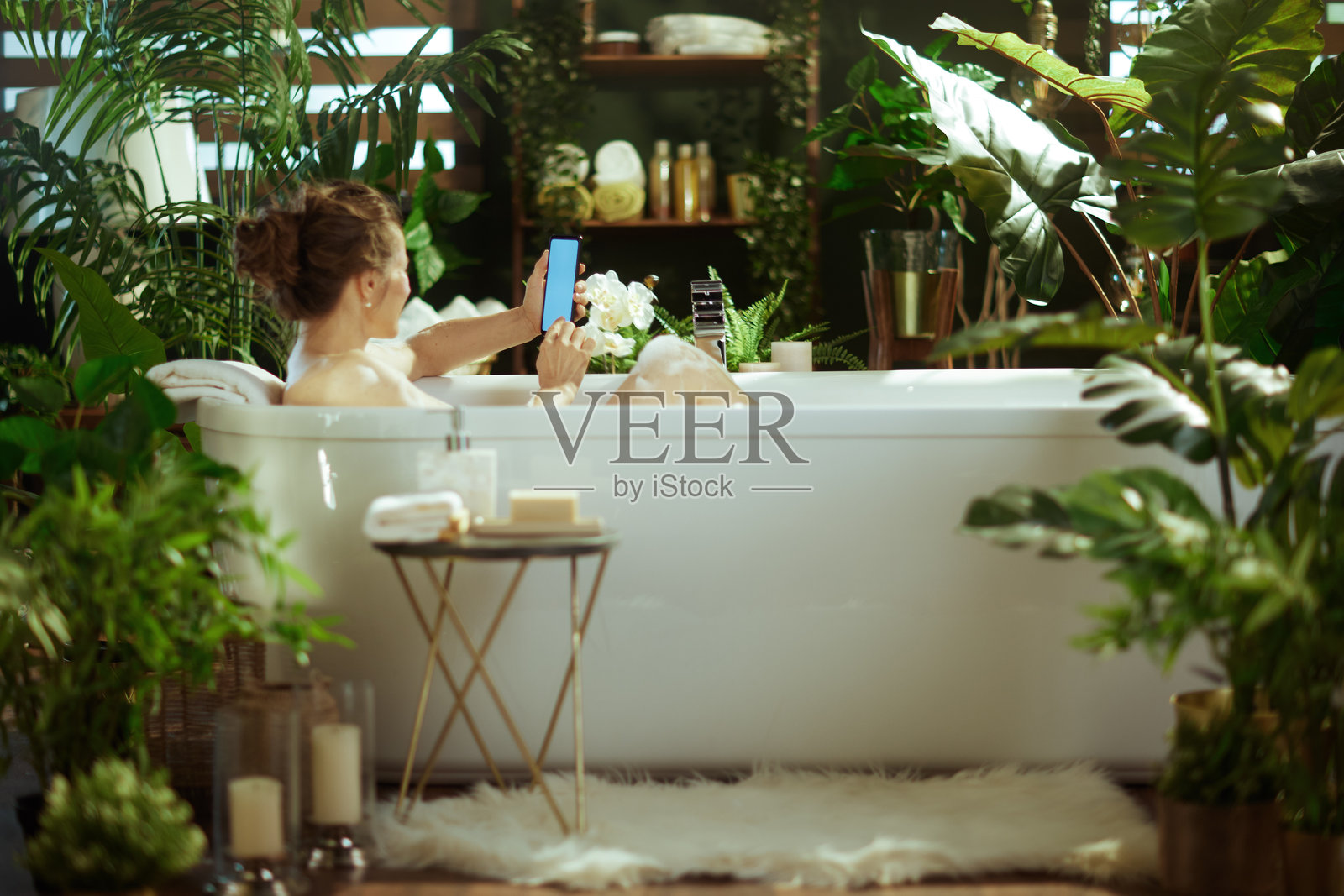 女人在绿植环绕的浴缸里放松地玩手机照片摄影图片