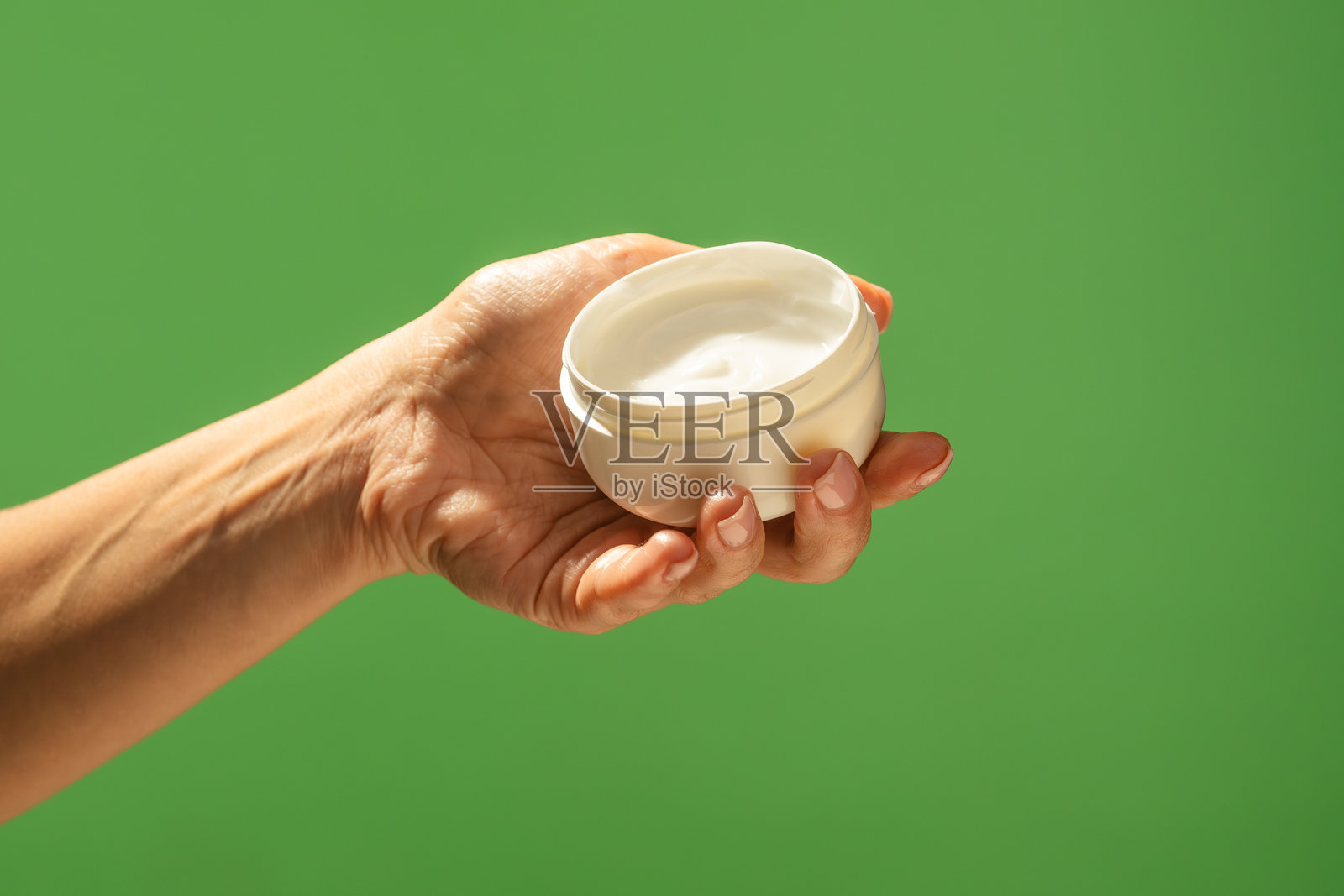手持白色乳霜罐，背景为绿色照片摄影图片