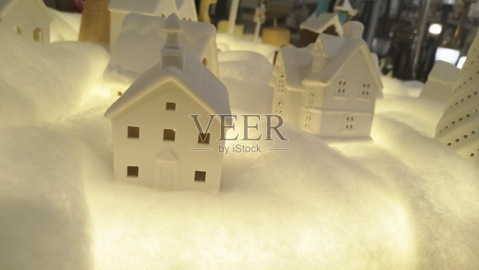 舒适的陶瓷微缩房屋，坐落于奇幻的雪景村庄展示中，房屋带有陡峭的屋顶、发光的装饰和柔和灯光下的微妙节日魅力。照片摄影图片