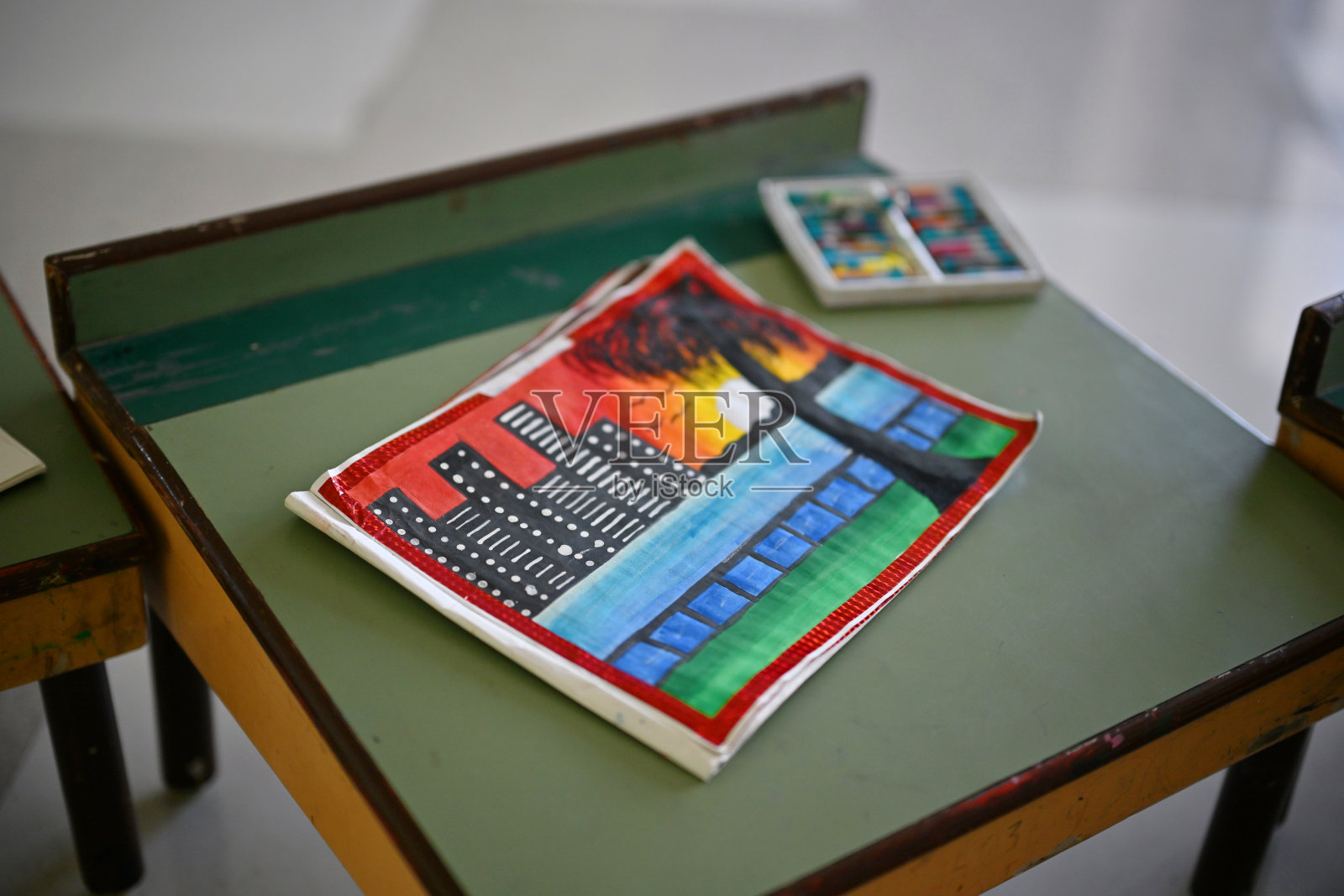 一张色彩斑斓的城市水景日落画作，摆放在教室的书桌上。照片摄影图片