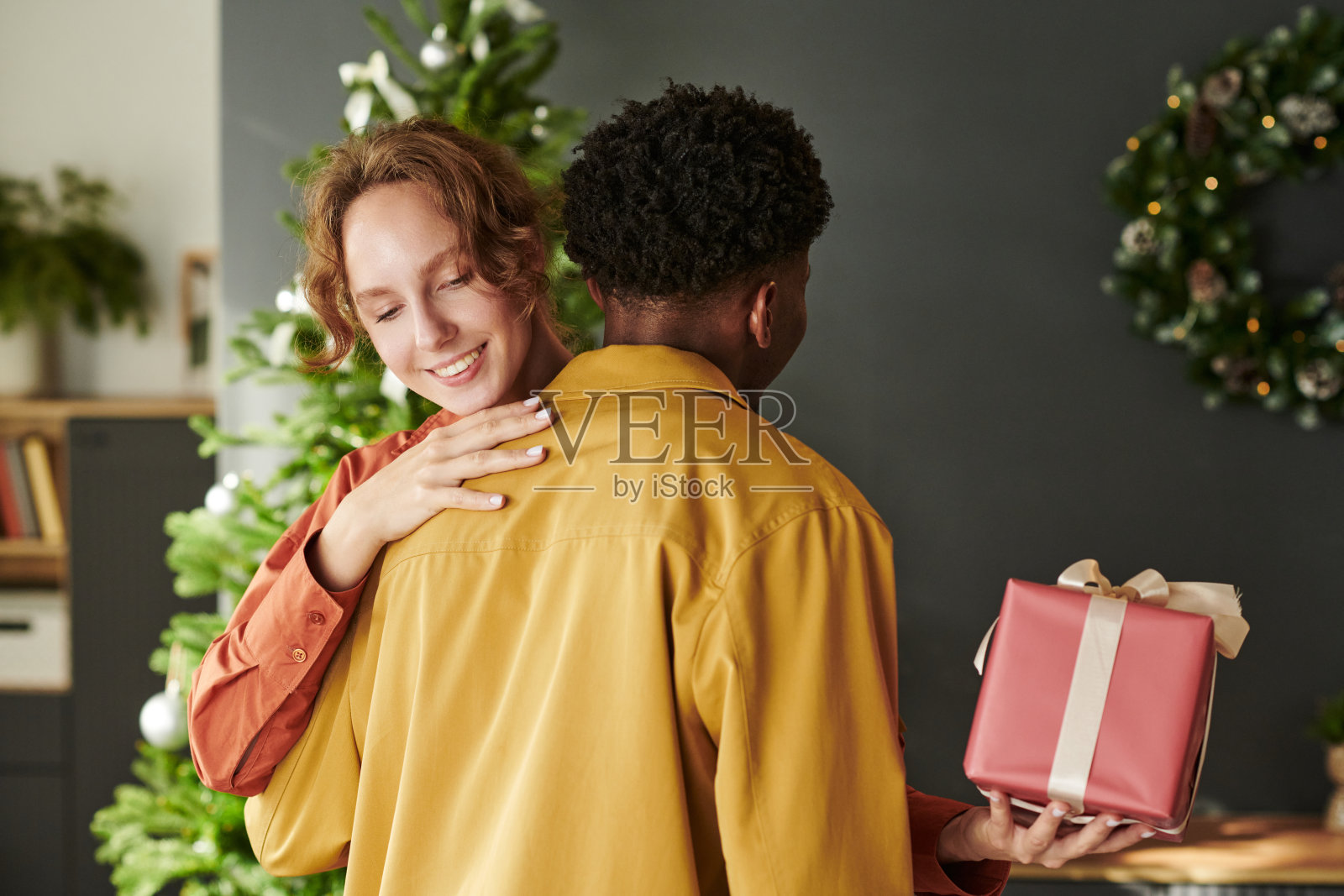 年轻女子在赠送圣诞礼物时拥抱年轻黑人男子照片摄影图片