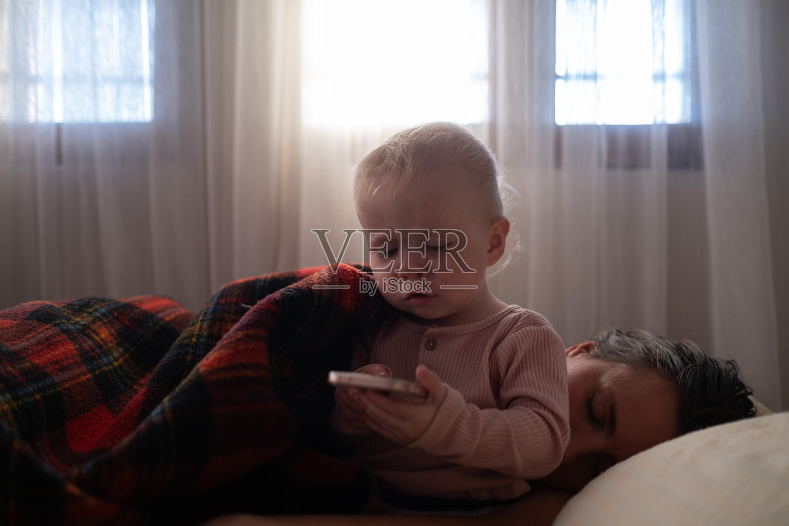 一个2岁的女孩躺在床上玩手机游戏。照片摄影图片