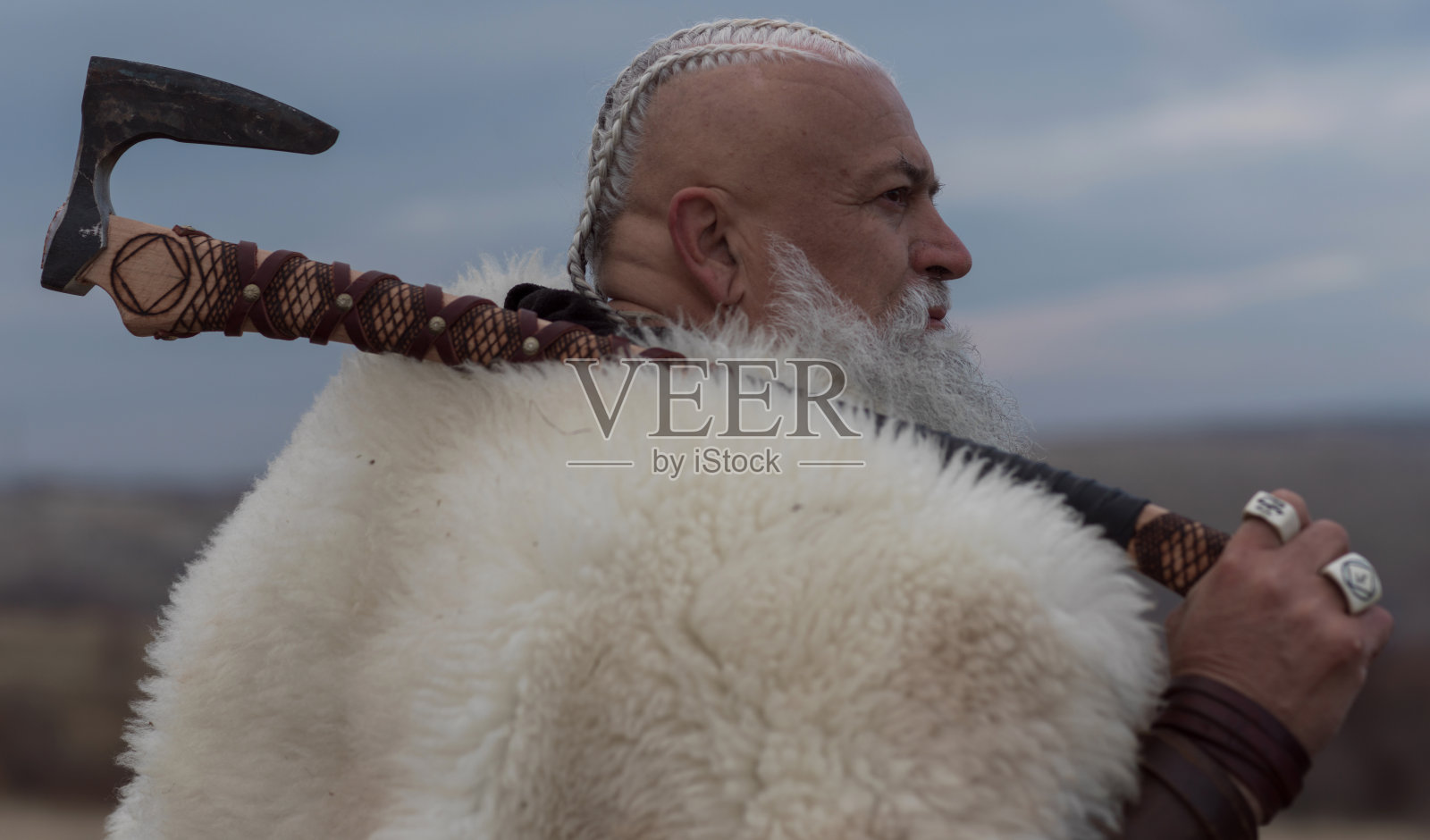 维京战士手持战斧，身披毛皮斗篷和皮甲，站在山崖上俯瞰壮丽的风景，这位北欧历史战士照片摄影图片