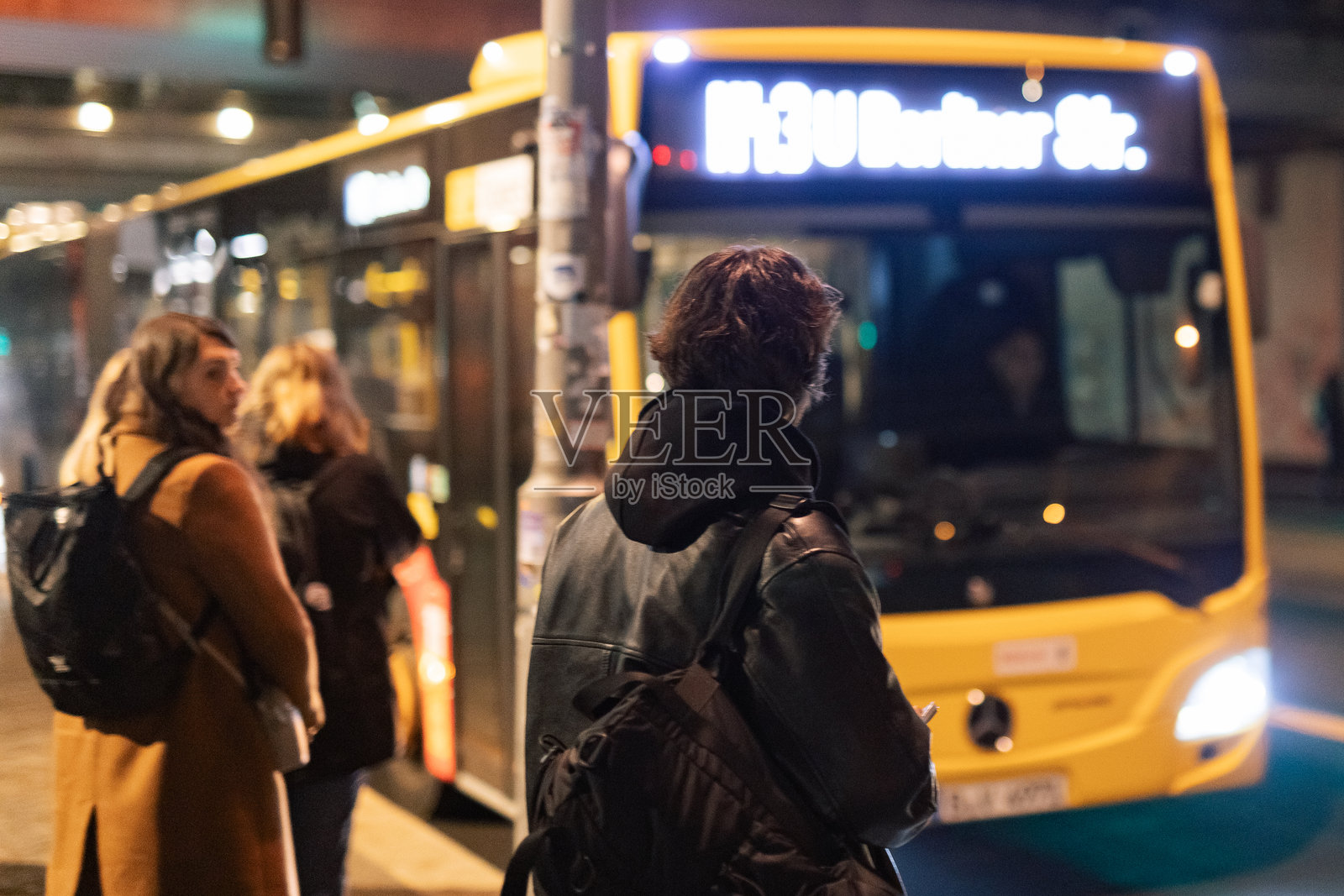 乘客在灯火通明的城市公交车站走近BVG M43路公交车照片摄影图片
