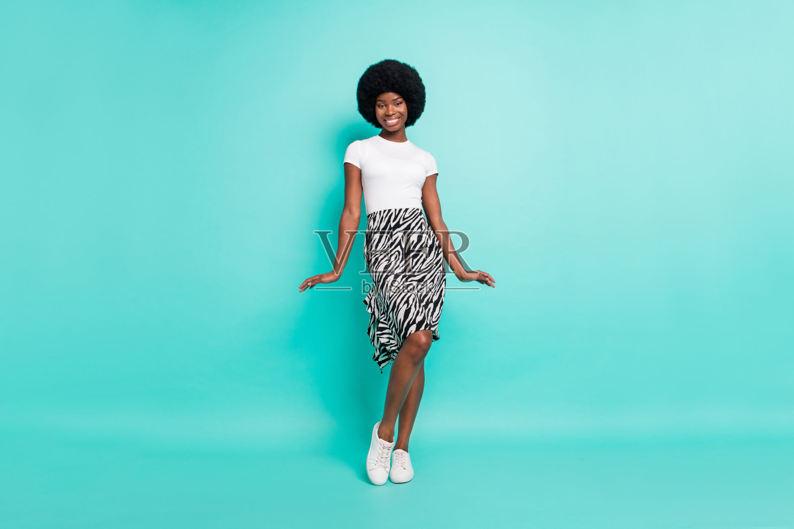 穿着休闲服的迷人害羞的深肤色女士，微笑着走动，背景是孤立的蓝绿色照片摄影图片