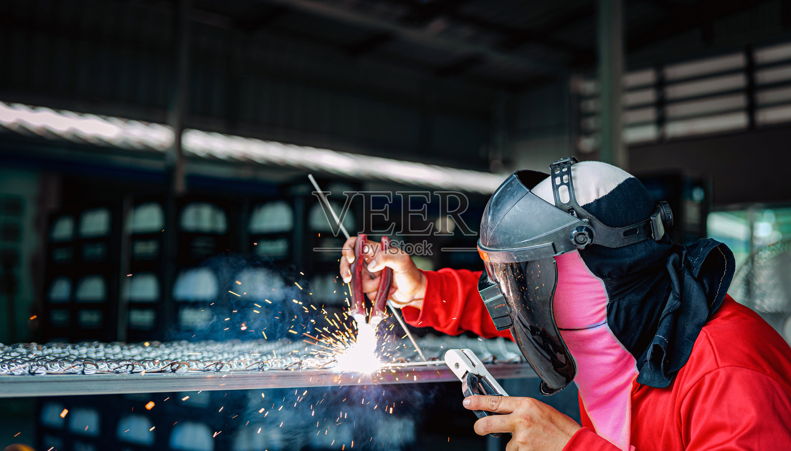 穿着红色长袖衬衫和防护面罩的焊工正在焊接钢格栅，工业焊工手持焊枪照片摄影图片