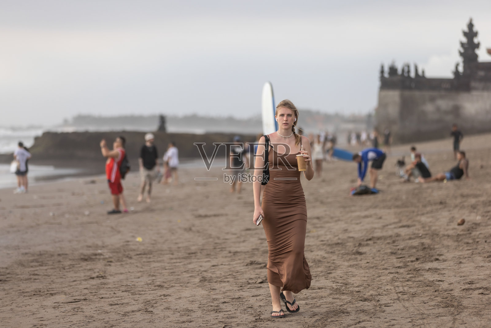 年轻的金发女子在日落时分的海滩上散步。照片摄影图片